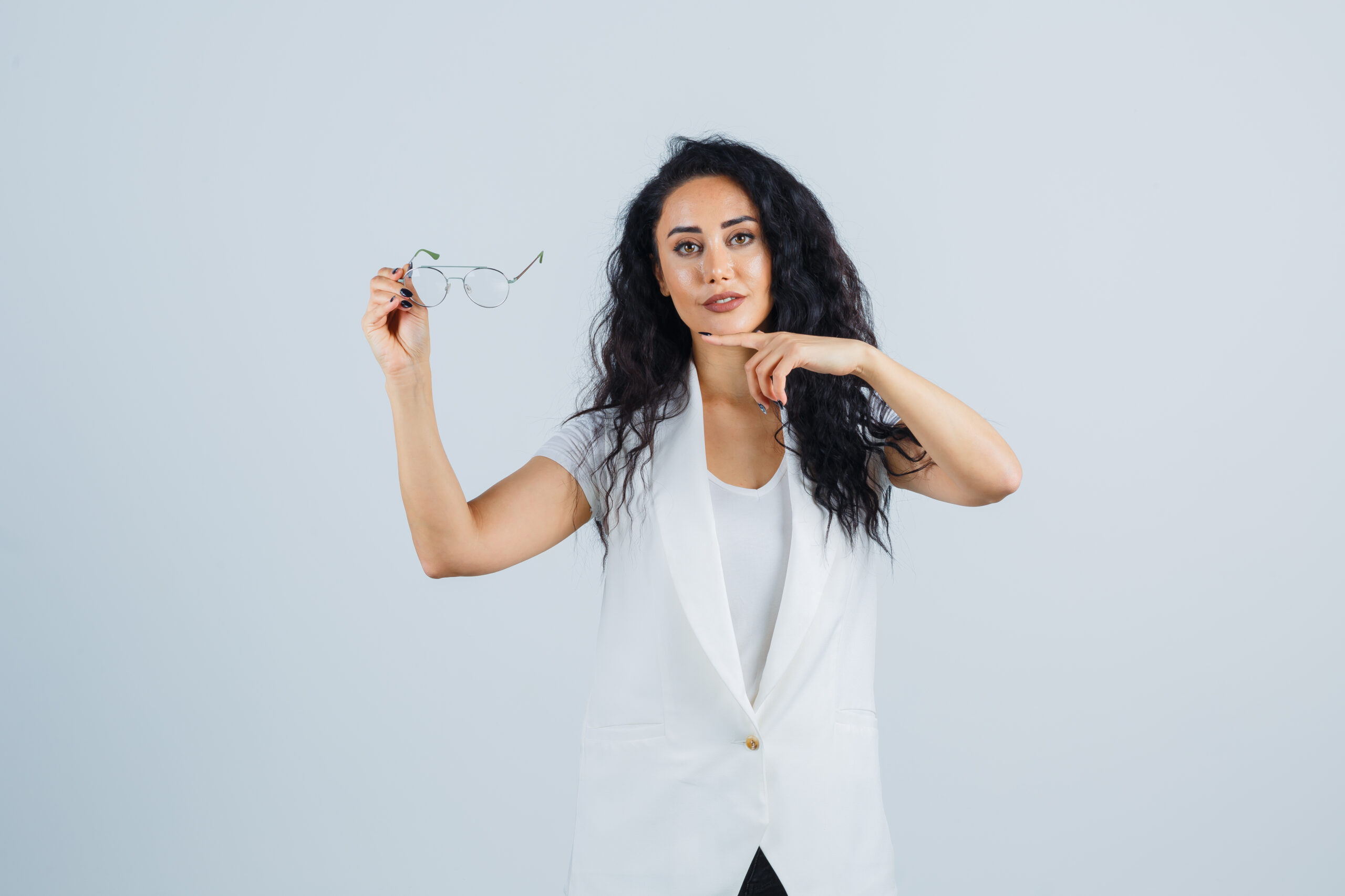 young lady pointing at glasses in white t shirt, jacket and looking confident , front view.